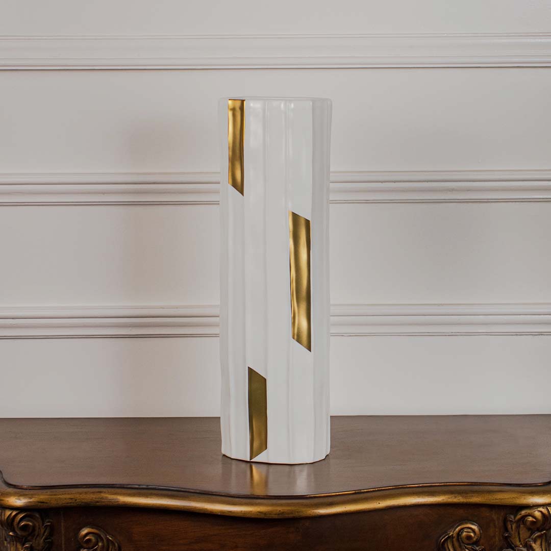 White faceted ceramic cylinder vase with gold geometric accents displayed on a vintage wood console table for luxury styling.
