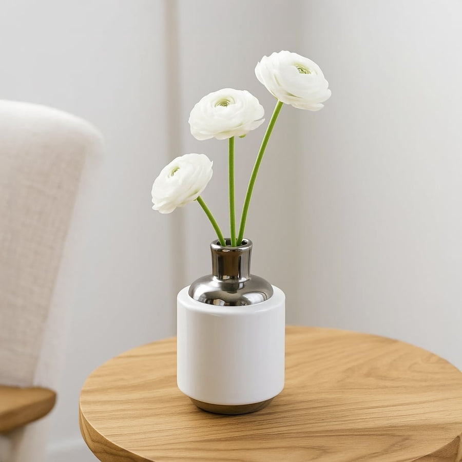 White ceramic vase with fresh white flowers placed on round wooden table creating clean minimal accent for modern home Decor.