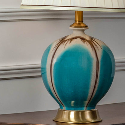 Closeup of turquoise ceramic table lamp with gold base and pleated white shade showing elegant design for luxury home lighting decor.