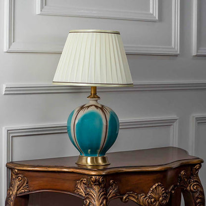 Turquoise ceramic table lamp with gold accents and pleated white lampshade illuminated on white background for modern home lighting.