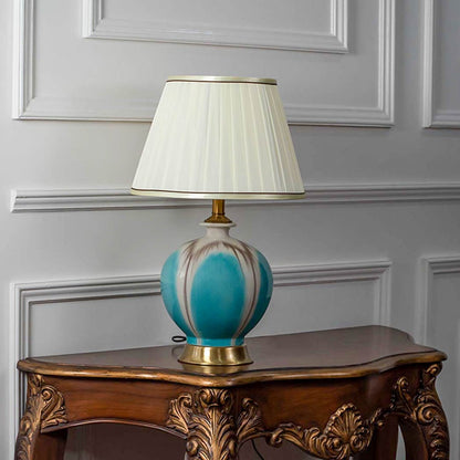 Teal glass table lamp with fabric shade styled on vintage console creating elegant lighting accent for living room decor.