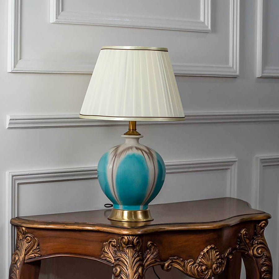 Teal glass table lamp with fabric shade styled on vintage console creating elegant lighting accent for living room decor.