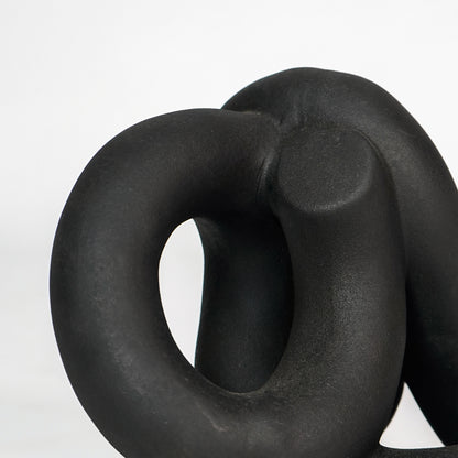 Closeup image of black resin abstract knot decor sculpture for modern shelf placement with smooth matte texture.