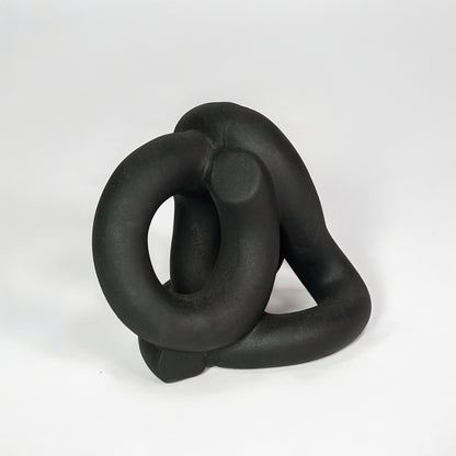 Black abstract ceramic decorative sculpture on white background for modern shelf decor styling.