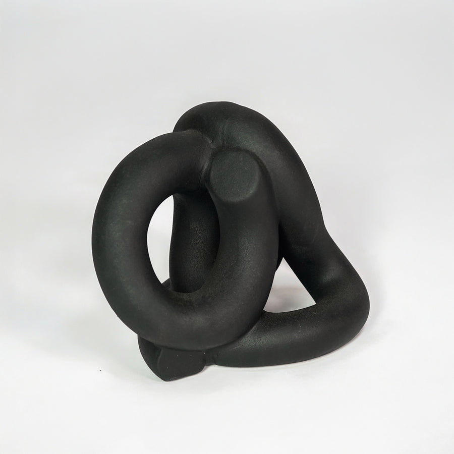 Black abstract ceramic decorative sculpture on white background for modern shelf decor styling.