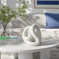 White abstract ceramic sculpture placed on modern coffee table with sofa background for stylish home decor.