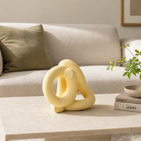 Yellow abstract ceramic sculpture placed on modern coffee table with sofa background for stylish home decor.
