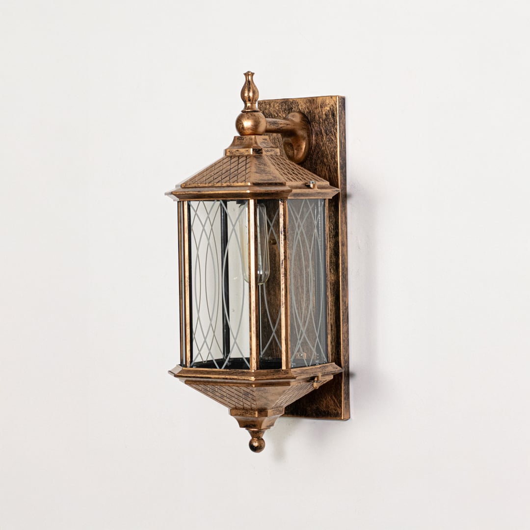 Antique gold metal outdoor wall lantern switched off on white background emphasizing detailed glass panels and metal finish.