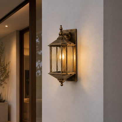 Antique brass metal outdoor wall light lifestyle image with a clear paneled glass lantern on a modern concrete wall.