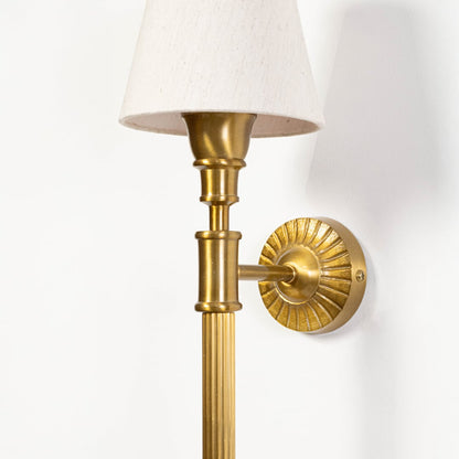 Detailed close up of brass wall light showing textured metal finish decorative backplate and elegant white lampshade construction.