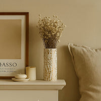 Tall white vase with gold accent panels displayed in a soft lifestyle setting adding a modern decorative touch to interior styling with its sleek vertical design.