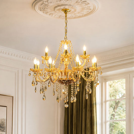 An ornate gold chandelier with hanging crystal droplets and candle-style bulbs, suspended from a decorative ceiling medallion in a bright room with white walls and a window.