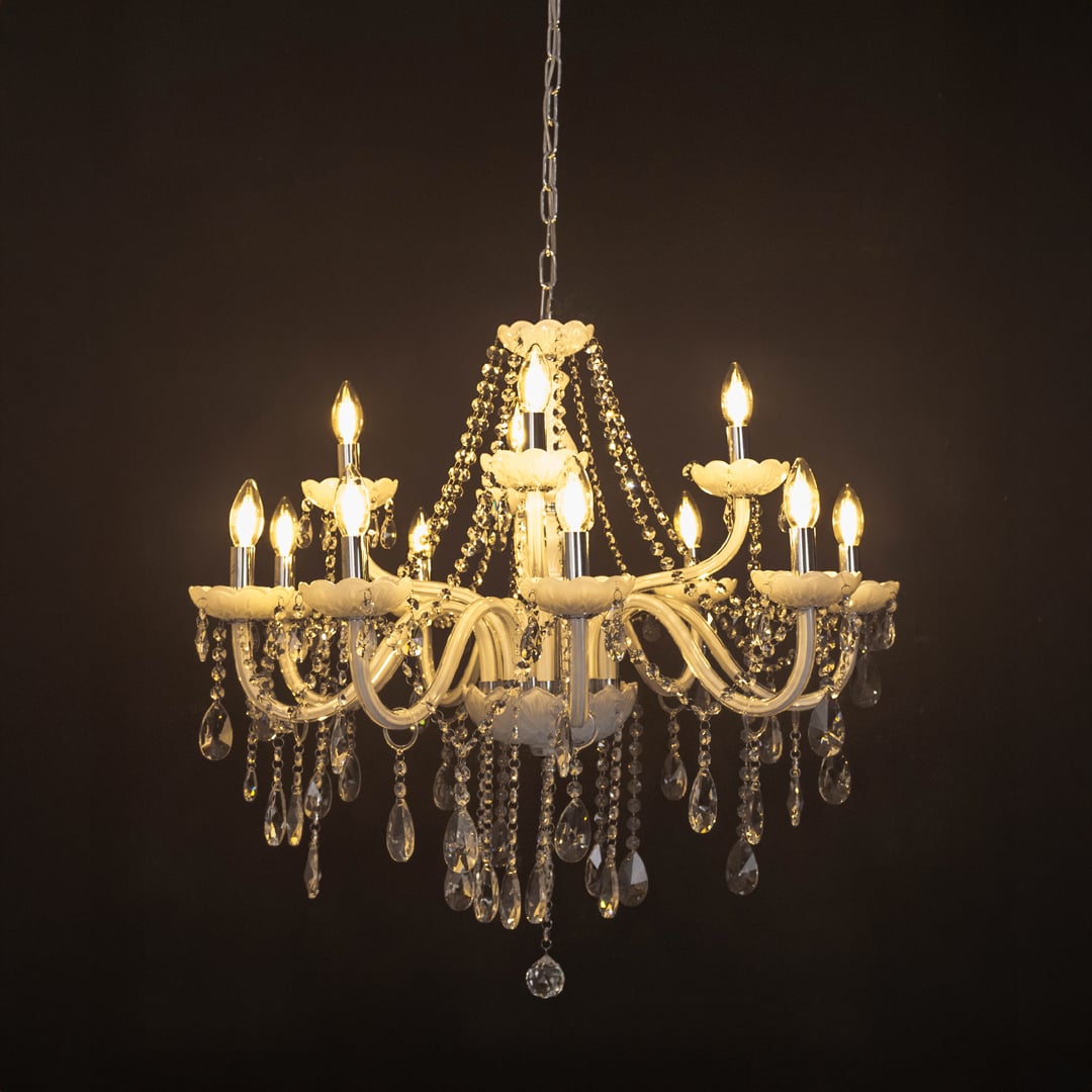 White chandelier with lights on glowing warmly with crystal accents and glass arms against a black background.