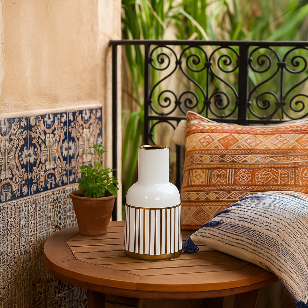 A white ceramic vase with gold striped detailing displayed on a wooden surface against a patterned wall creating a refined modern decor look.