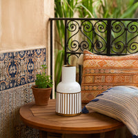A white ceramic vase with gold striped detailing displayed on a wooden surface against a patterned wall creating a refined modern decor look.