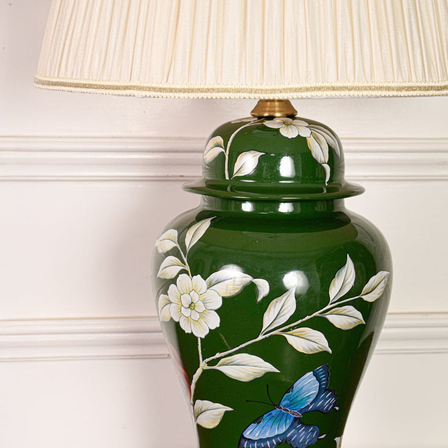 Closeup of green ceramic table lamp highlighting hand painted floral butterfly details glossy glaze finish and gold metal base.