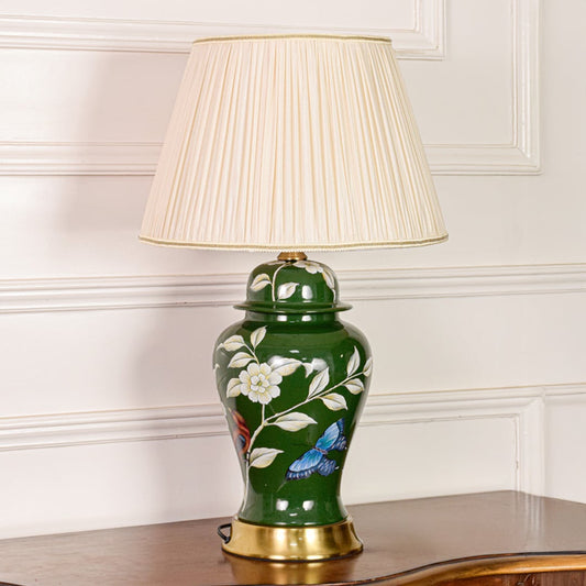 Decorative green ceramic table lamp with floral butterfly artwork gold metal base and pleated fabric shade on off white background.
