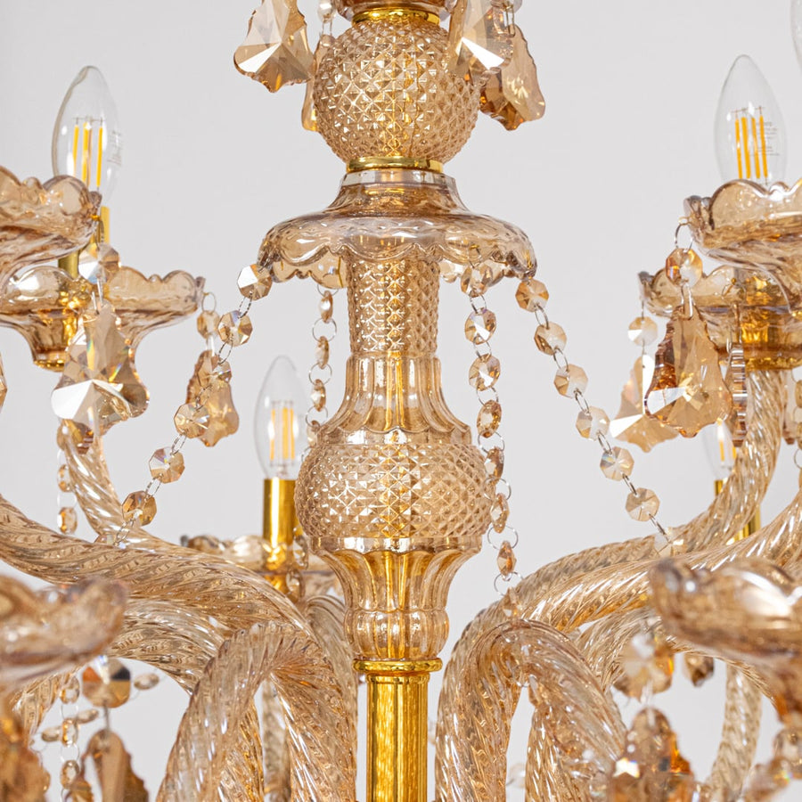 Closeup of golden chandelier showing crystal chains candle style bulbs and detailed glass body for home decor.