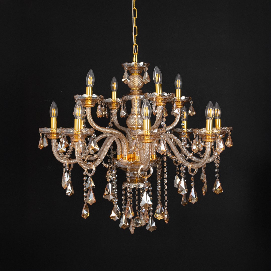 Golden chandelier with lights off highlighting crystal drops and glass arms against a black background.