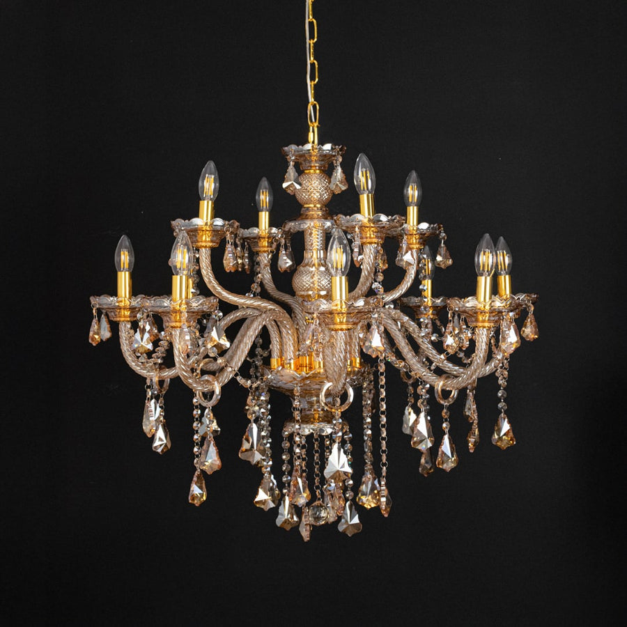 Golden chandelier with lights off highlighting crystal drops and glass arms against a black background.