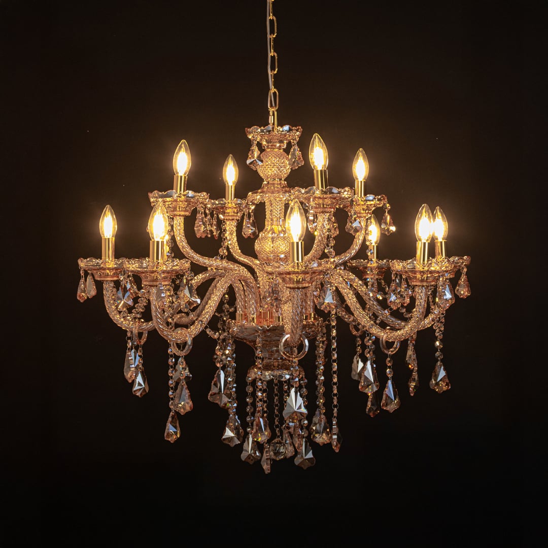 Golden chandelier with lights on glowing warmly with crystal accents photographed on black background.