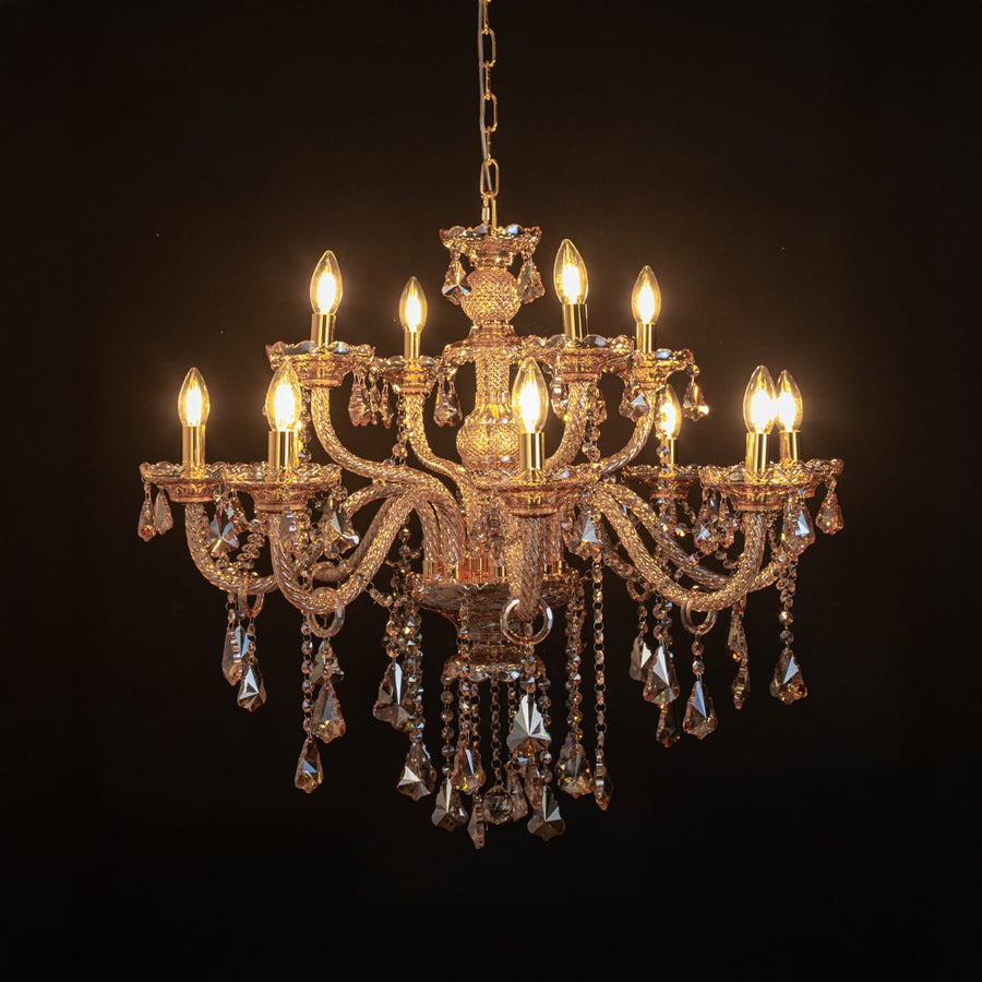 Golden chandelier with lights on glowing warmly with crystal accents photographed on black background.