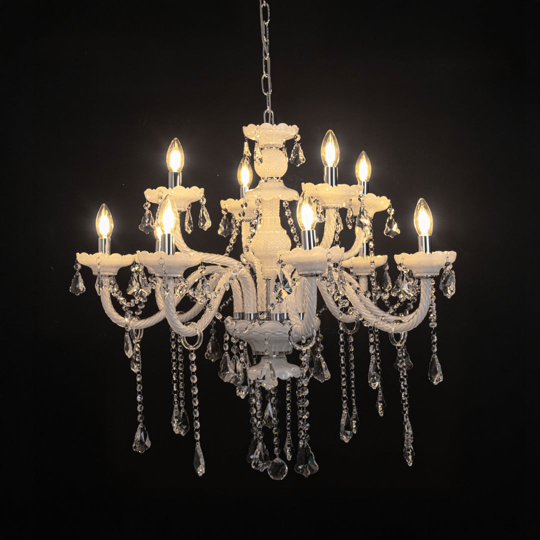 White chandelier with lights on glowing warmly with crystal drops and glass body against a black background.