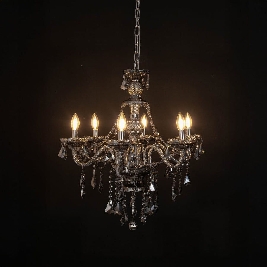 Chandelier illuminated with warm lights against a black background highlighting crystal design.