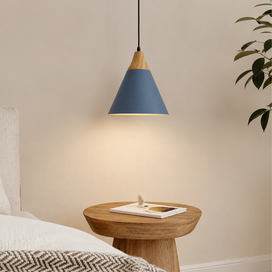 A modern pendant lamp with a blue-gray cone shade and natural wood accents, hanging above a round wooden bedside table in a softly lit bedroom setting.