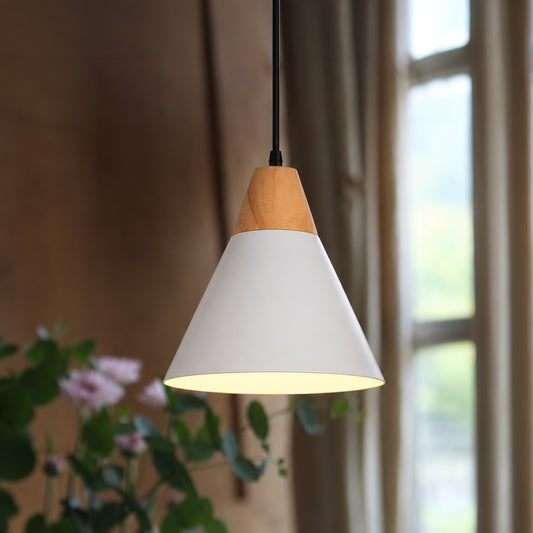 A modern cone-shaped pendant light with a white metal shade and a natural wood accent at the top, hanging in a softly lit room with a window and blurred greenery in the background.