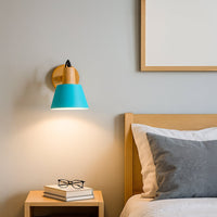 Wall mounted bedside light with turquoise shade and wooden base creating a warm reading glow beside a modern bed and nightstand in a calm minimalist bedroom setting.