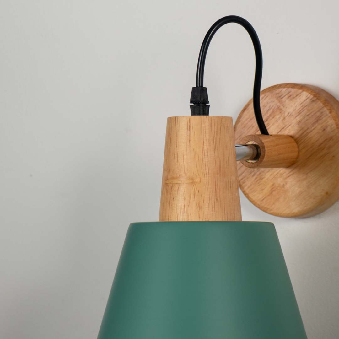 Green metal wall light with wood finish mount and black curved arm on neutral background minimal modern lighting for bedroom decor.