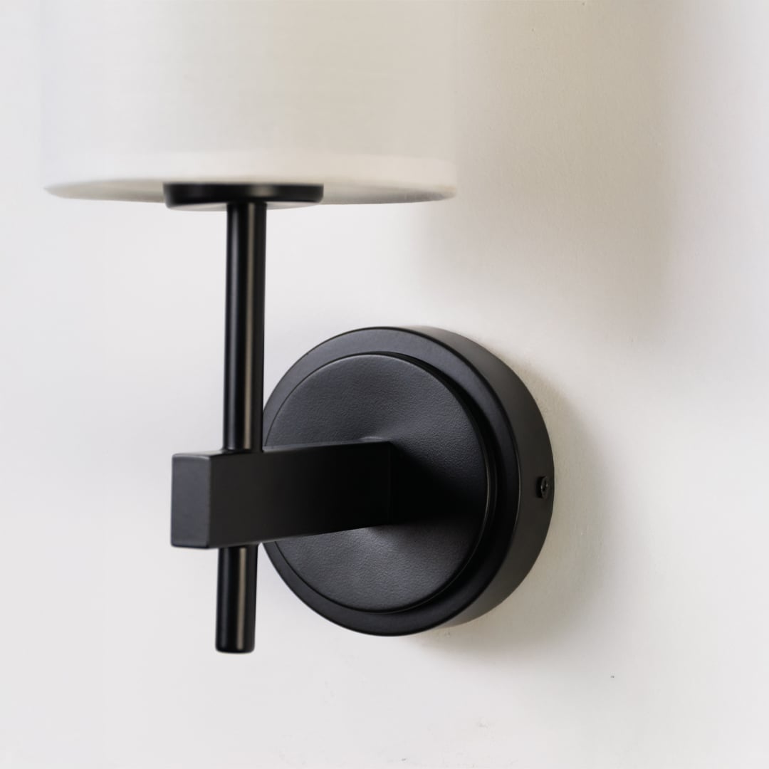 Closeup of black metal wall light with tall white fabric shade showing premium detailing for modern indoor lighting in stylish home interiors.