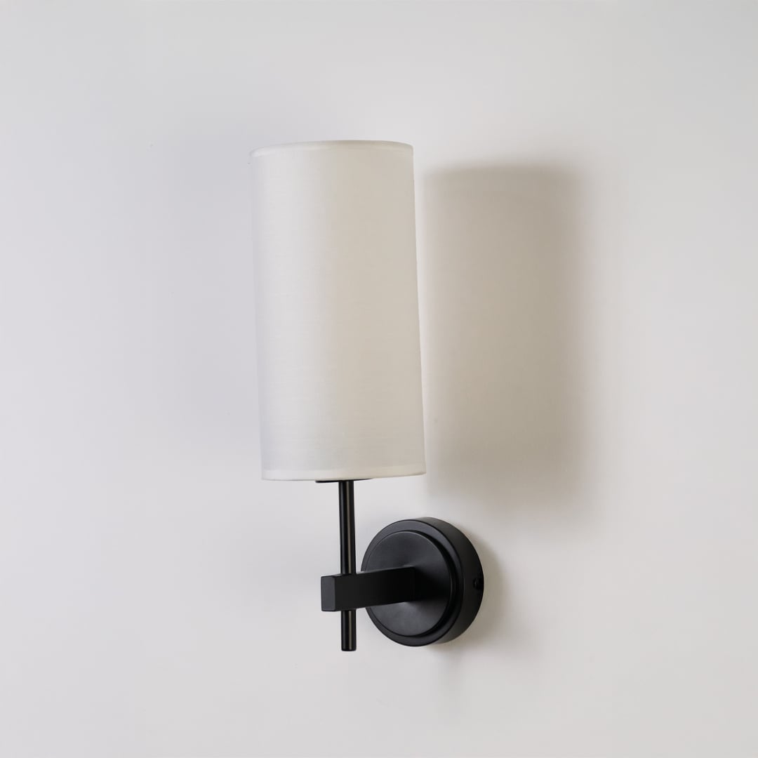 Black metal wall light with tall white fabric shade shown on a clean white background with light off highlighting its sleek modern design.