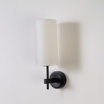 Black metal wall light with tall white fabric shade shown on a clean white background with light off highlighting its sleek modern design.