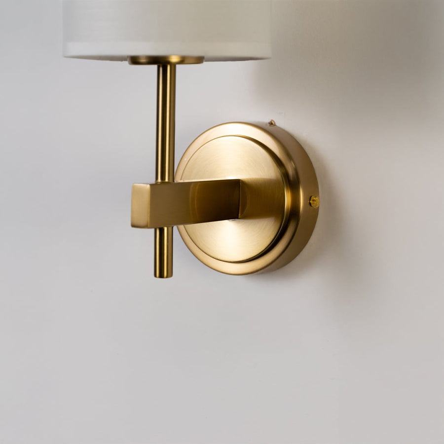 Closeup of gold metal wall light with tall white fabric shade showing refined detailing for premium indoor lighting in modern home interiors.