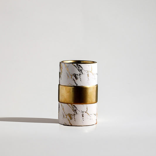 White ceramic cylinder vase featuring black and gold marble veins accented with a thick polished brass band in the center.