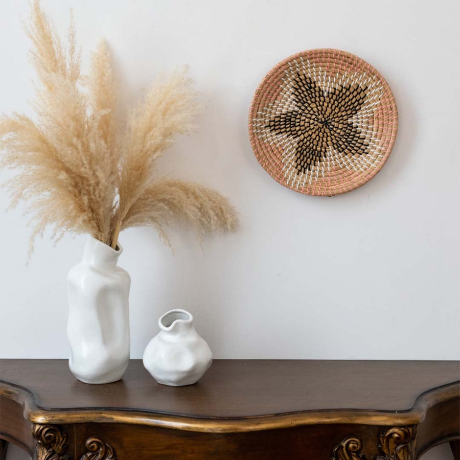Handwoven wall basket decor in natural pink and black fiber styled above wooden console table for boho wall.