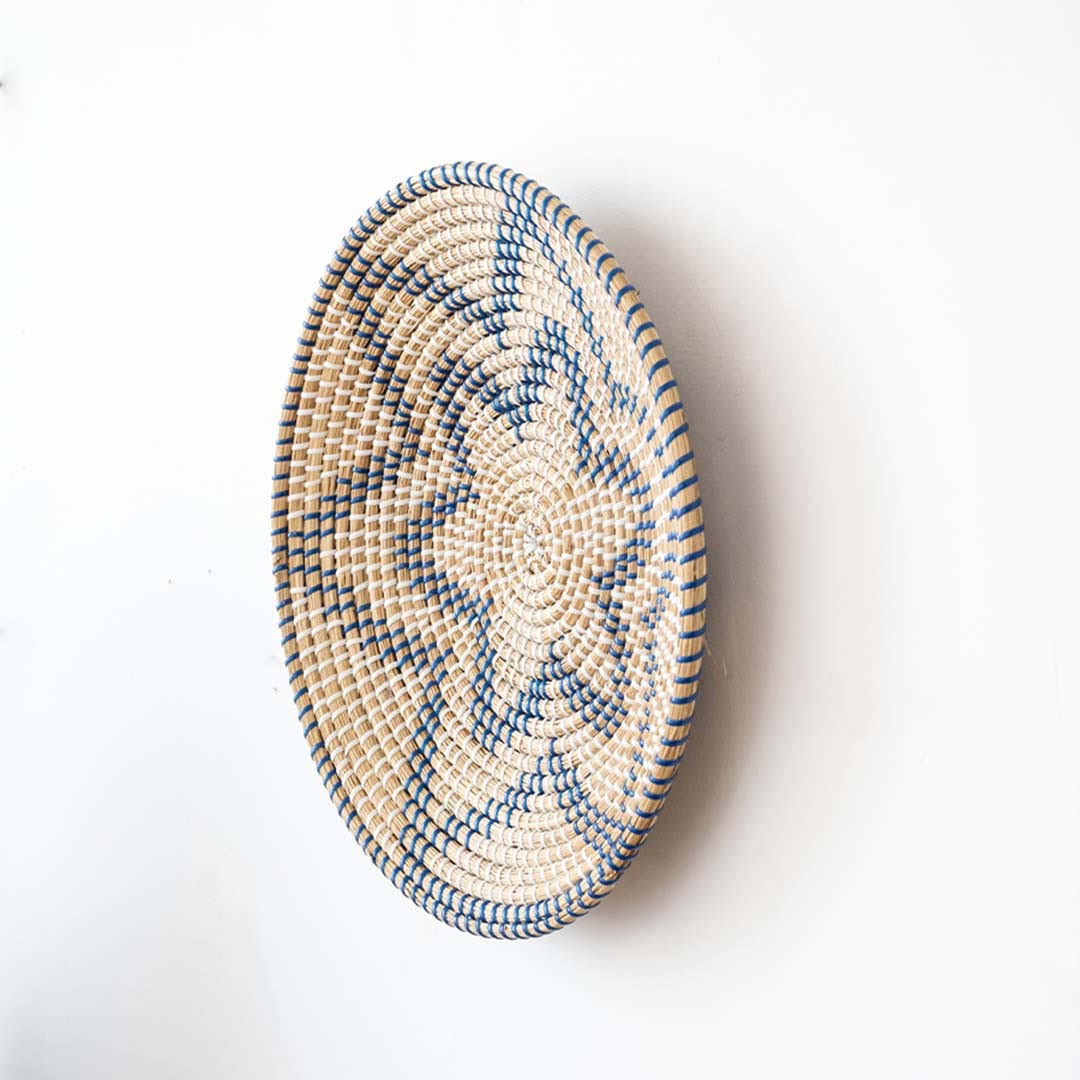 Side angle view of a star pattern black woven seagrass wall hanging basket plate showing depth details on a white wall.