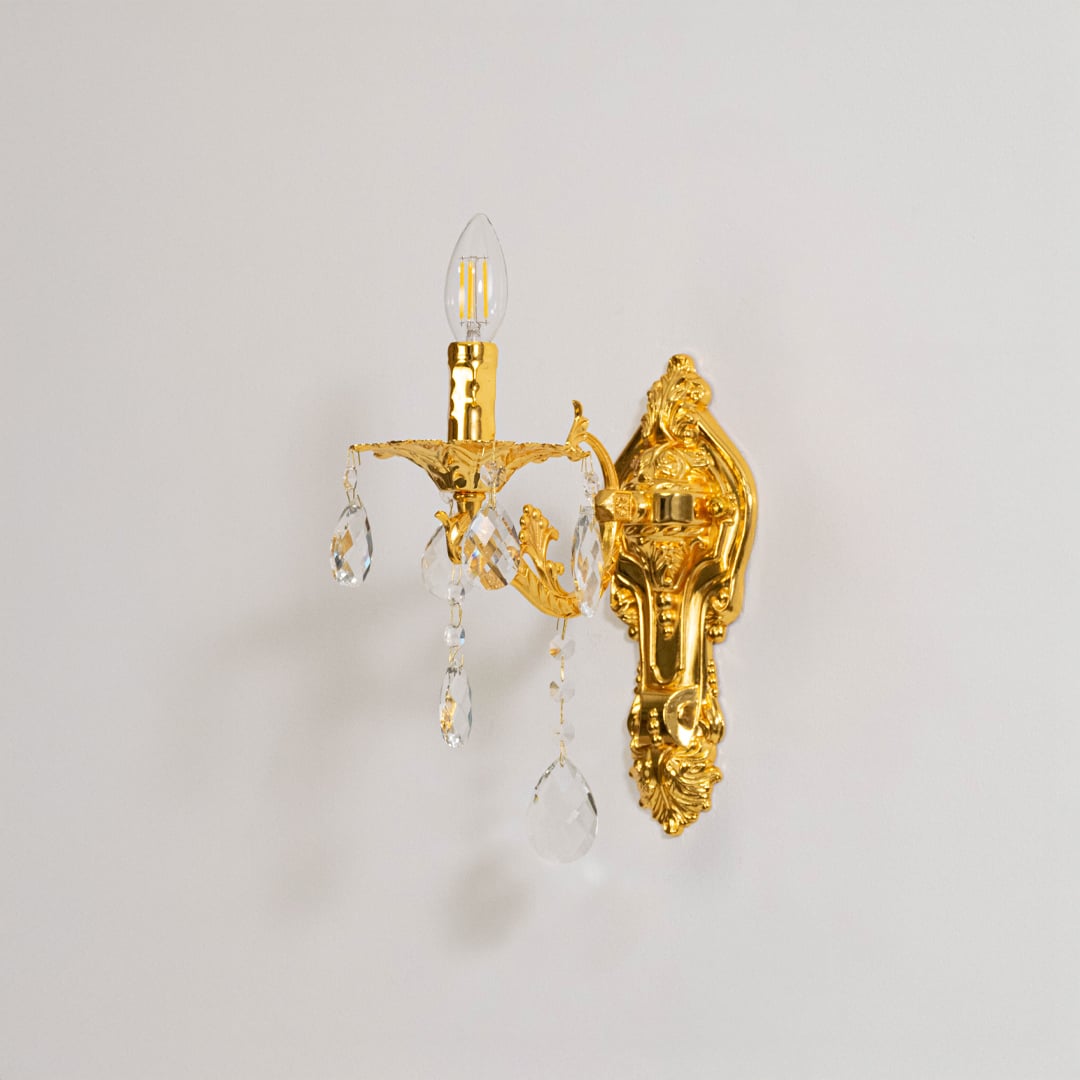 Golden wall light with crystal drops classic candle style wall mounted decorative lighting on off white background.