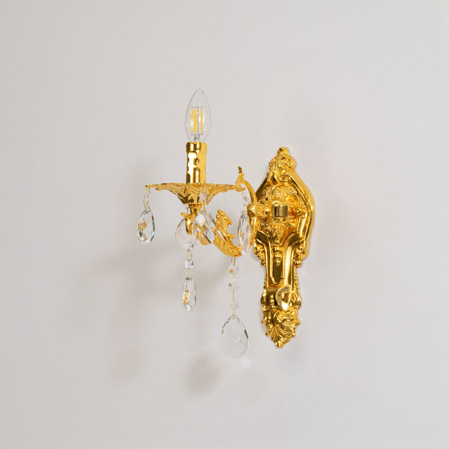 Golden wall light with crystal drops classic candle style wall mounted decorative lighting on off white background.