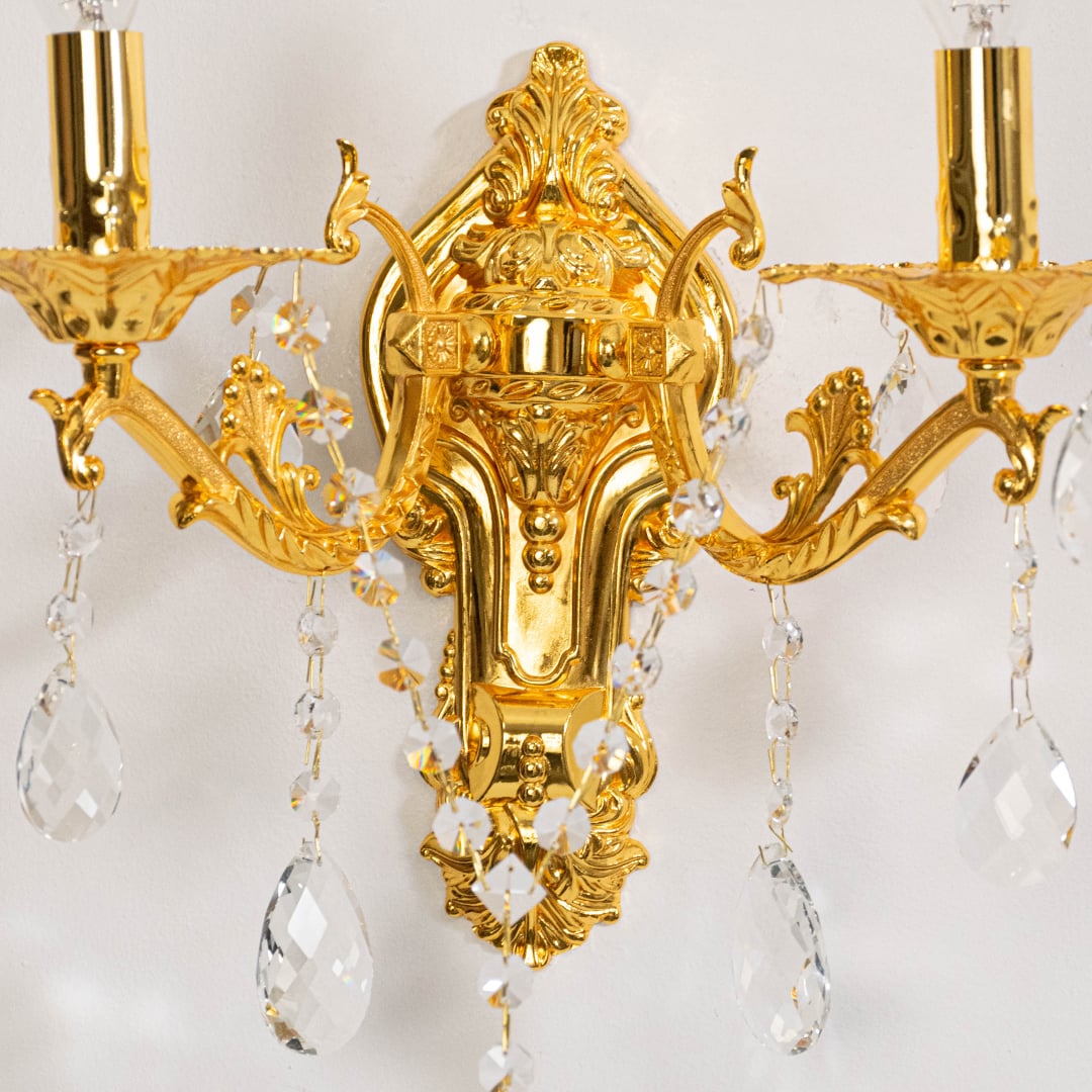 Closeup of golden wall light with crystal drops dual candle style decorative fixture for luxury home interiors.