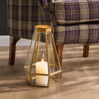 Luxury gold geometric faceted glass panel lantern floor candle holder sitting on a hardwood floor next to a purple plaid armchair.