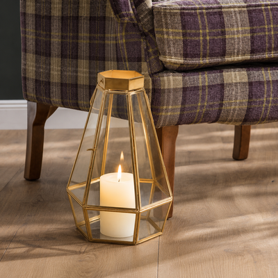 Luxury gold geometric faceted glass panel lantern floor candle holder sitting on a hardwood floor next to a purple plaid armchair.