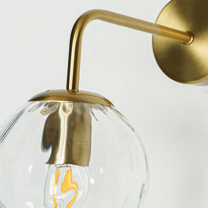 Modern brass wall light with clear textured glass globe and elegant curved arm for luxury interiors.