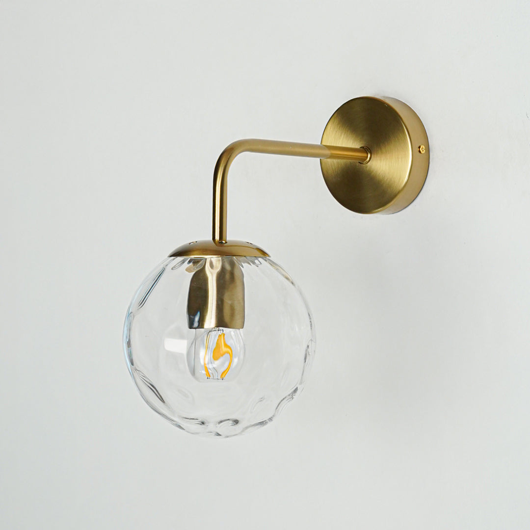 Elegant brass wall light with clear textured glass globe for modern interior wall lighting decor.