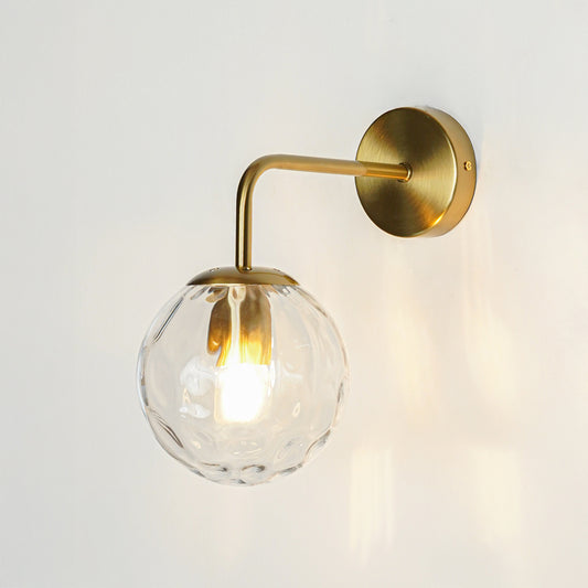 Modern brass wall light with clear textured glass globe creating warm elegant interior lighting decor.