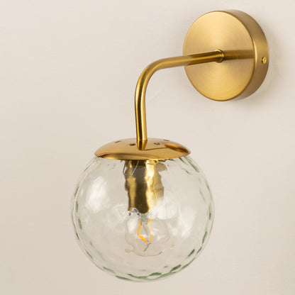 Contemporary brass metal wall light with textured clear glass globe for stylish bedroom and hallway decor.