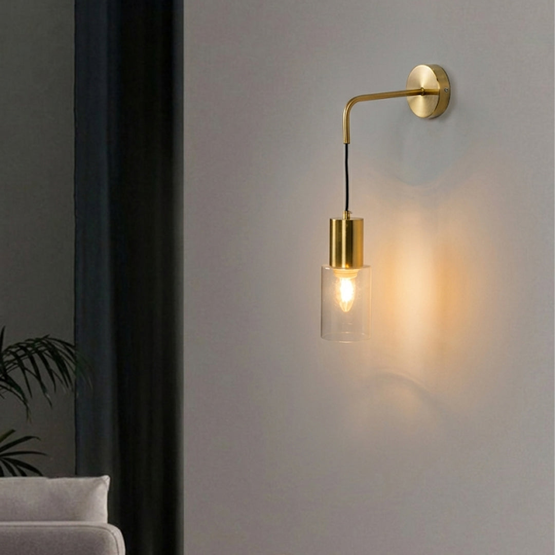 Glowing brass wall light fixture with hanging glass shade against white wall in a living room