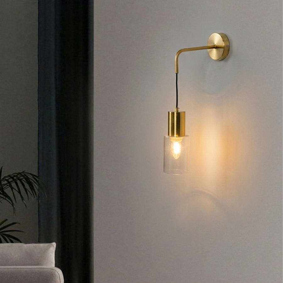 Glowing brass wall light fixture with hanging glass shade against white wall in a living room